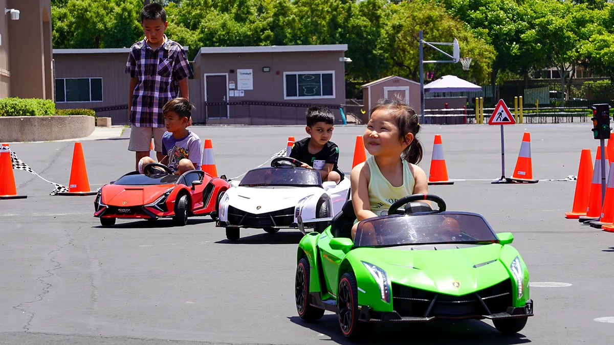 Three young kids smiling as they drive green, white and red Little Racers OC branded ride-on Lamborghinis around a coned racetrack in Orange County
