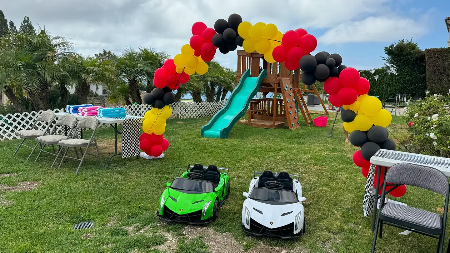 A backyard racing birthday party set up by Little Racers OC with a balloon arch, checkered-flag runners and green and white branded ride-on Lamborghinis