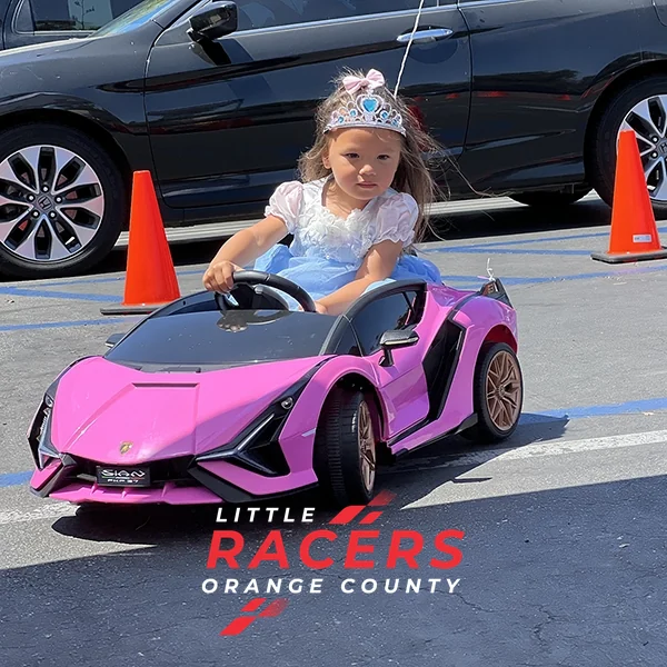 A little girl wearing a princess tiara driving a pink branded ride-on Lamborghini